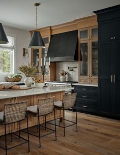 a kitchen with black cabinets and white counter tops, wooden flooring and hanging lights over the island