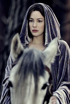 a woman in a hooded robe riding on the back of a white and black horse