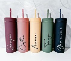 six different colored travel mugs with the names of their respective people on them, all lined up in a row