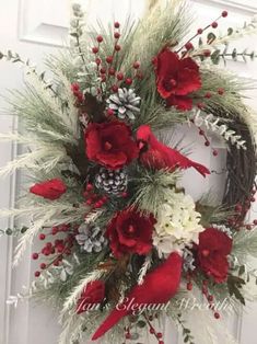 a wreath with red and white flowers is hanging on a door handle, decorated with pine cones