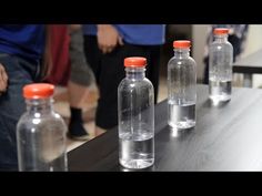 three empty glass bottles sitting on top of a wooden table with people standing in the background