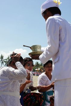 a group of people standing on top of a beach next to each other holding a bowl