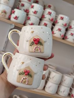 two coffee mugs decorated with holly and candy canes are held in front of shelves full of cups