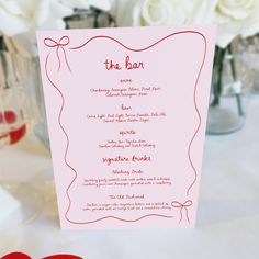 a pink menu card sitting on top of a table next to two red heart shaped napkins