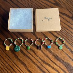 six bracelets with charms sitting on a wooden table next to a box that says raspberry lane