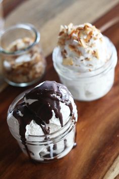 two jars filled with ice cream and toppings on top of a wooden table next to each other