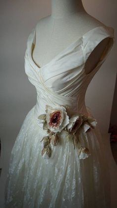 a white dress with flowers on the waist and shoulder, sitting on a mannequin