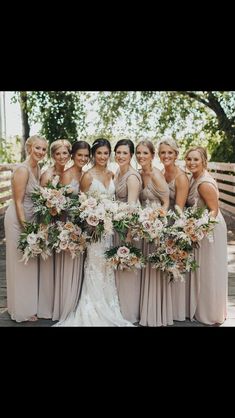 a group of women standing next to each other in front of a wooden fence holding bouquets