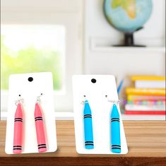 two pairs of earrings are sitting on a shelf in front of a globe and window