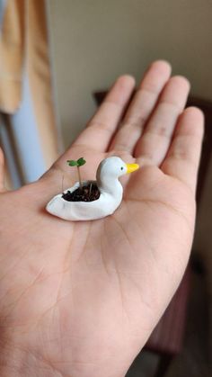 a hand holding a tiny white duck with a plant in it's beak,