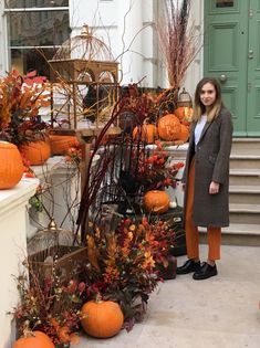 a woman standing in front of a building with pumpkins and plants on the steps