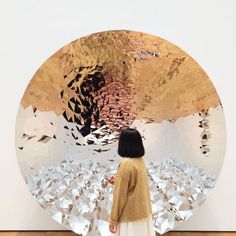 a woman standing in front of a large mirror with many objects on the wall behind her