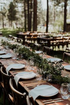 a long wooden table with place settings and greenery on it in the middle of a forest