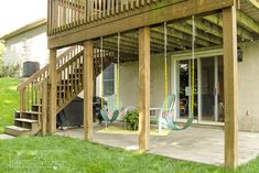 a porch with swings and chairs on the front lawn, next to a deck that has stairs leading up to it