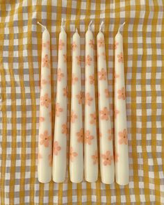 four candles are lined up on a checkered tablecloth with flowers painted on them