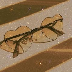 a pair of heart shaped glasses sitting on top of a shiny surface with stars in the background