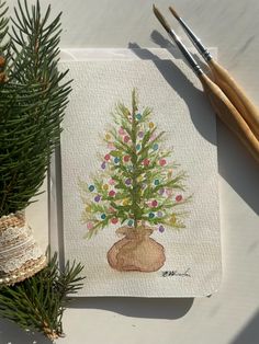 a painting of a small christmas tree on a piece of paper next to some needles