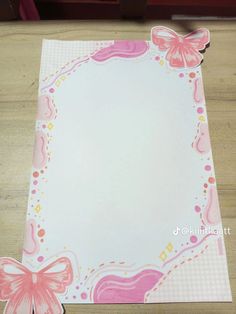 a pink and white paper with butterfly decorations on the edges, sitting on a wooden table