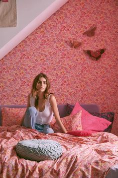 a woman sitting on top of a bed next to a pink wallpapered room