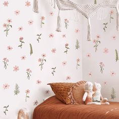 a teddy bear sitting on top of a bed next to a wall with pink flowers