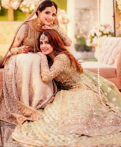 two women in wedding outfits posing for the camera with one woman sitting on her lap