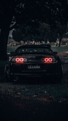 the back end of a black sports car parked in front of a tree at night