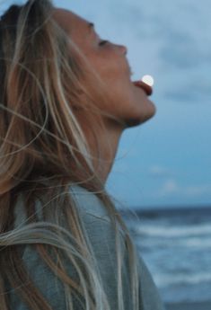 a woman standing on the beach with her eyes closed looking up at something in the sky