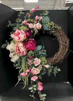 a wreath with pink flowers and greenery hanging from the front of a black wall