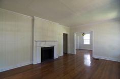 an empty living room with hard wood floors and white paint on the walls, along with a fireplace