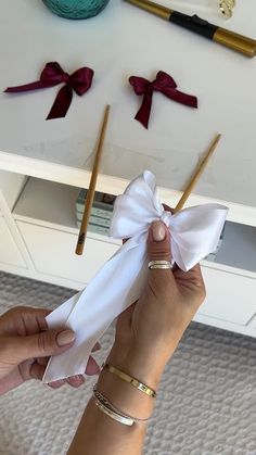 a woman holding up a white bow on top of a piece of cloth next to some knitting needles