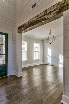 an empty living room with wood floors and white walls, chandelier hanging from the ceiling