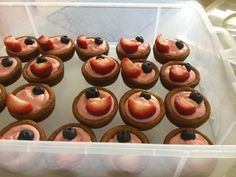 a plastic container filled with cupcakes covered in frosting and strawberries on top