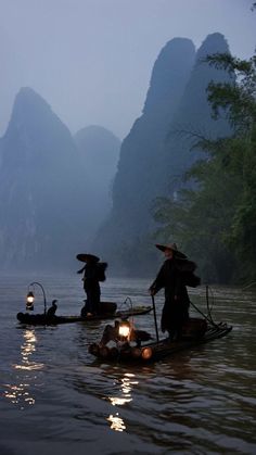 two people on small boats in the water with mountains in the backgrouds