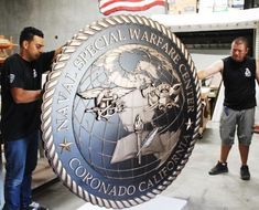 two men standing in front of a sign that says the special warrant office corcondado california