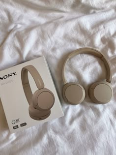 the sony wireless headphones are next to its box on a white sheeted bed