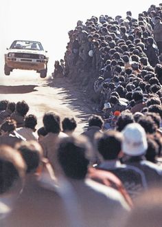 a large group of people standing in front of a truck on a dirt road next to a crowd of people