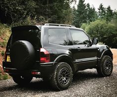 a black suv parked on the side of a dirt road next to some trees and bushes