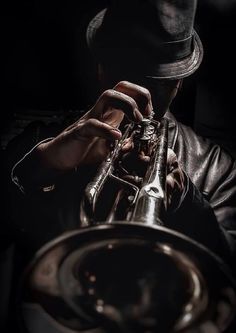 black and white photograph of a man playing a trumpet in the dark with his hat on