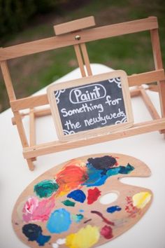 a wooden easel sitting on top of a white table covered in paint and paper