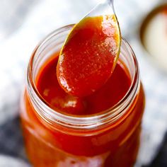 a spoon full of ketchup sitting on top of a jar filled with sauce