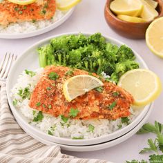 two white plates topped with fish and broccoli next to lemon wedged rice