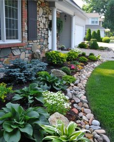 a garden with rocks and flowers in front of a house