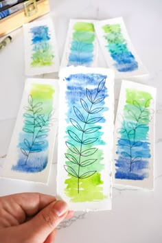 four watercolor paintings on paper with one being held up to show the different colors