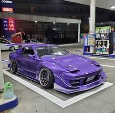 a purple sports car parked in a parking lot next to a gas station with no one around