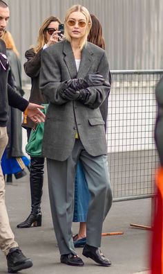 the woman is walking down the street in her gray suit and black gloves, with one hand on her shoulder