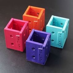 four different colored plastic containers sitting on a black surface with holes in the middle and bottom