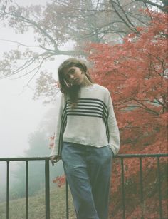 a woman standing next to a fence talking on a cell phone while wearing blue pants