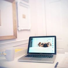 an open laptop computer sitting on top of a white desk next to a cup and pen