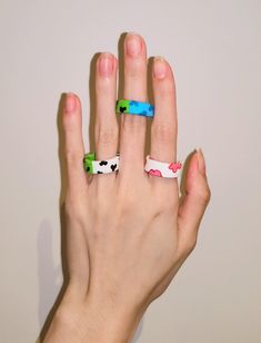 a person's hand with three different colored rings on their fingers and one is wearing a cow print ring