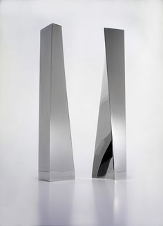 two tall silver vases sitting next to each other on a white surface with reflections